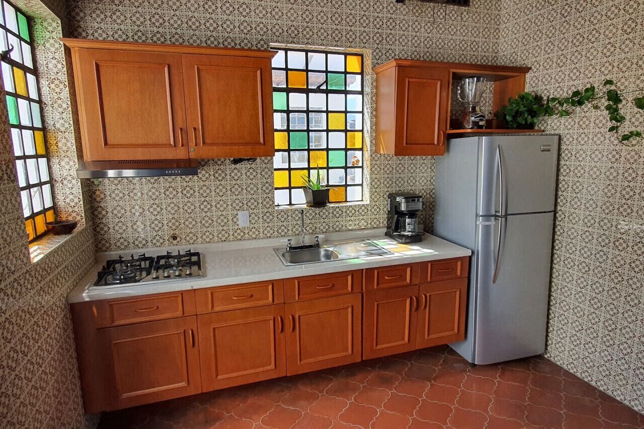 A kitchen with wooden cabinets, a stainless steel refrigerator, a gas stove, and a window with colorful glass panes.