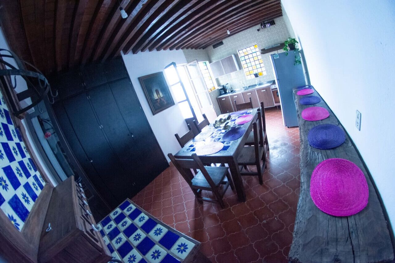 A dining area with a wooden table and chairs, a tiled floor, and a wooden bench with colorful cushions.