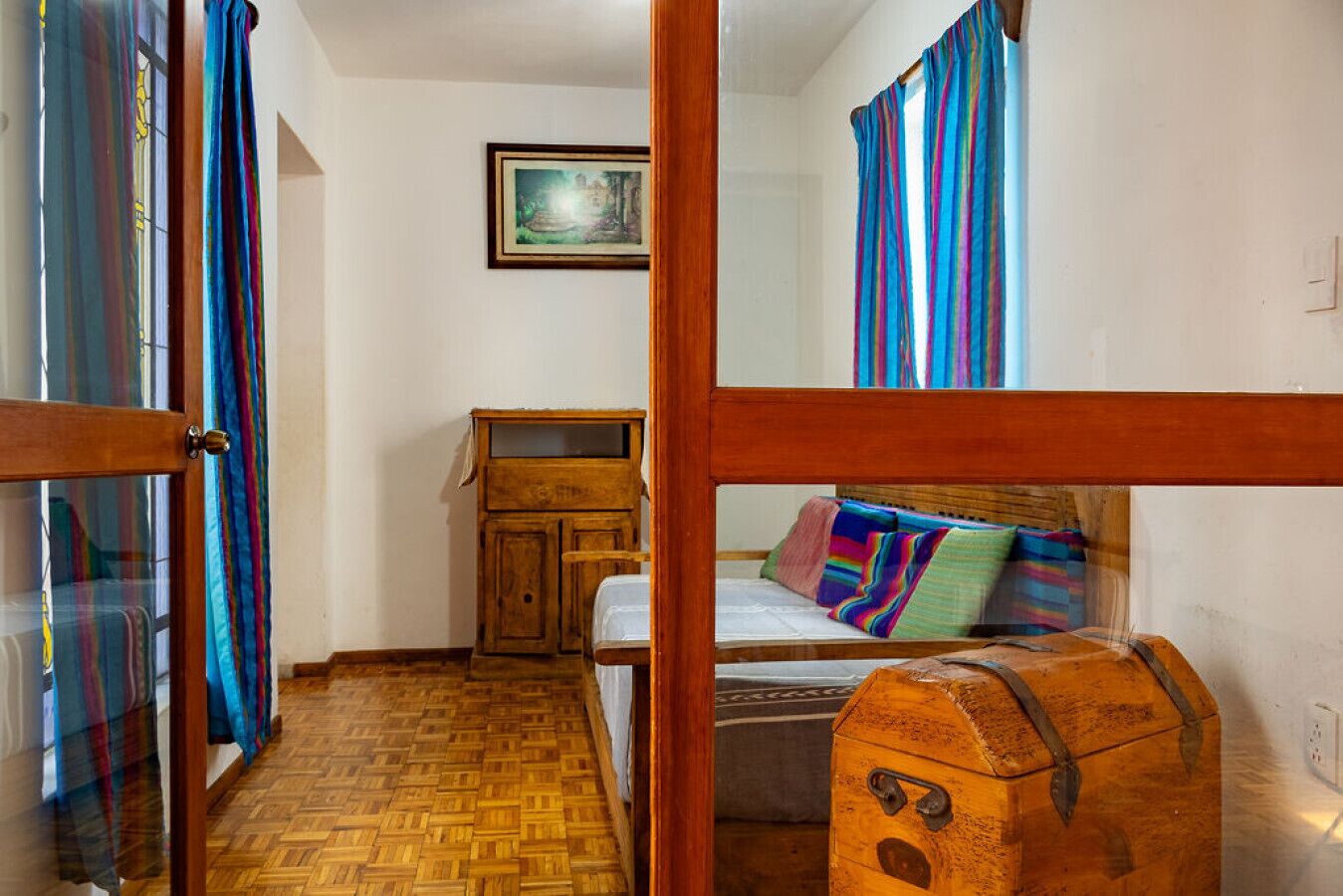 Quarto com cama de madeira, cómoda, mesinha e um quadro pendurado na parede.
