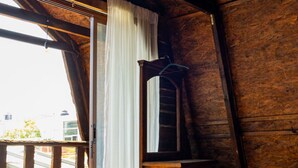 A rustic wooden room with a sloped ceiling, a bed, a wooden dresser, and a window with curtains. - Troje tradicional purépecha - live the experince (Morelia)