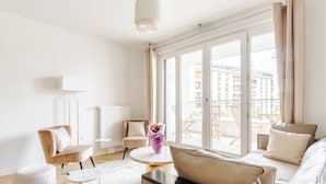 A modern living room with a sofa, armchairs, a round coffee table, and a view of the city through large windows. - Appart. Victoria(sleeps 7, 2 parking spaces)- Les Demoiselles à Versailles (Versailles)