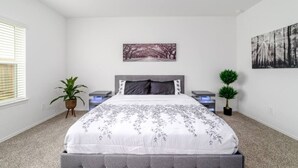 A bedroom with a large bed, two bedside tables, a wall-mounted artwork, and a potted plant. - Freshly Built 4BR, 2.5-Bath Home in North Houston (Houston)