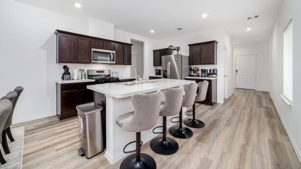 A modern kitchen with dark wood cabinets, stainless steel appliances, and a central island with bar stools. - Freshly Built 4BR, 2.5-Bath Home in North Houston (Houston)