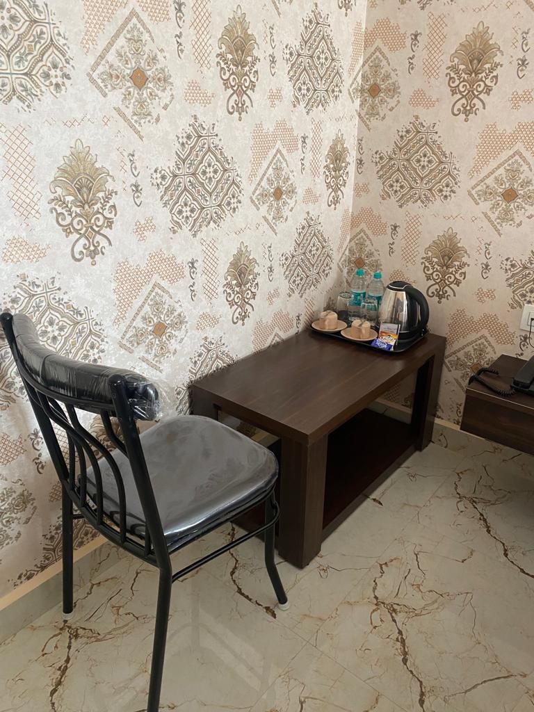 Un pequeño comedor con una mesa de madera y una silla negra. Hay una bandeja con comida y una tetera sobre la mesa. Las paredes tienen un papel tapiz estampado.