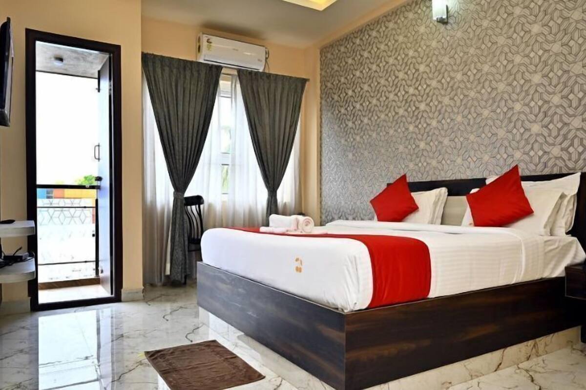 A hotel room with a bed, a TV, a balcony, and an air conditioning unit.