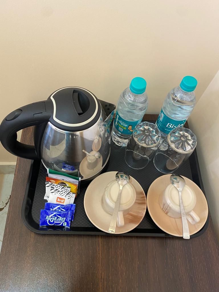A tray with a kettle, two bottles of water, two glasses, two plates with spoons, and some food packets.