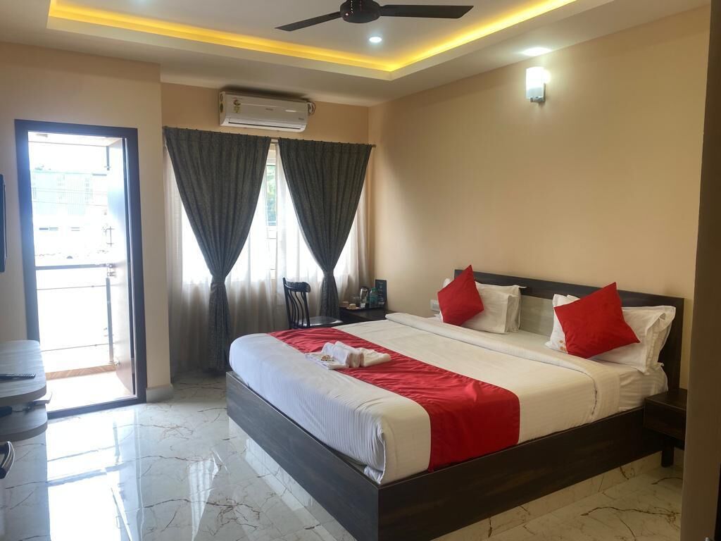 A hotel room with a large bed, a ceiling fan, an air conditioning unit, and a view through a door.