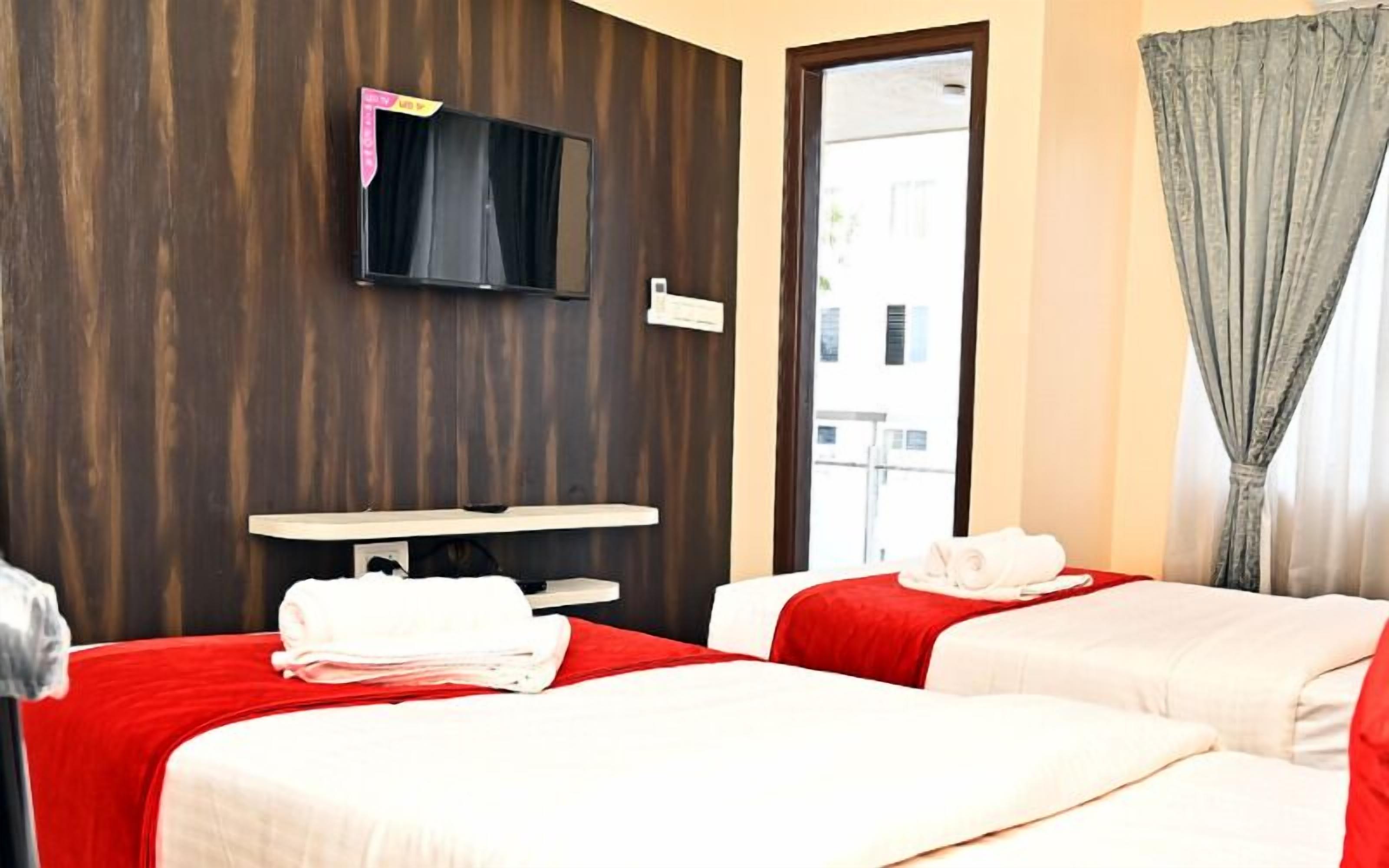 Une chambre d’hôtel avec deux lits, un téléviseur fixé au mur, une petite table et une fenêtre avec des rideaux.