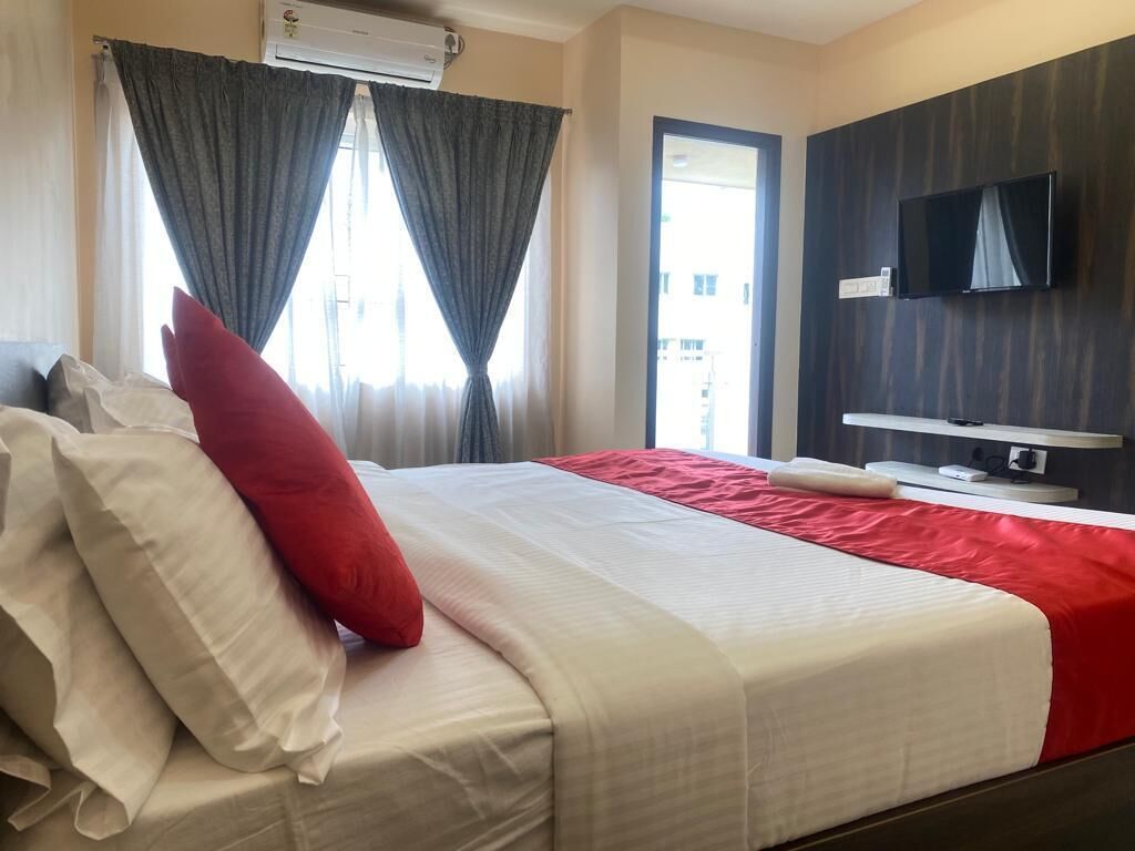 A hotel room with a bed, curtains, a TV, and an air conditioning unit.