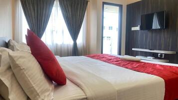 A hotel room with a bed, curtains, a TV, and an air conditioning unit.