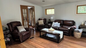 A living room with a brown leather sofa, a leather armchair, a coffee table, and a wooden floor. - Waterfall View from Secluded 4 Bed Cabin in East Branch, NY with Mountain Views (East Branch)