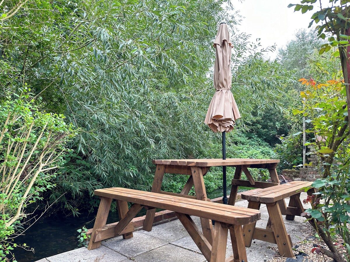 Une table de pique-nique en bois, avec un parasol, dans un jardin.
