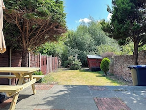 Un jardin avec une table de pique-nique, un petit abri de jardin et un mur en briques.