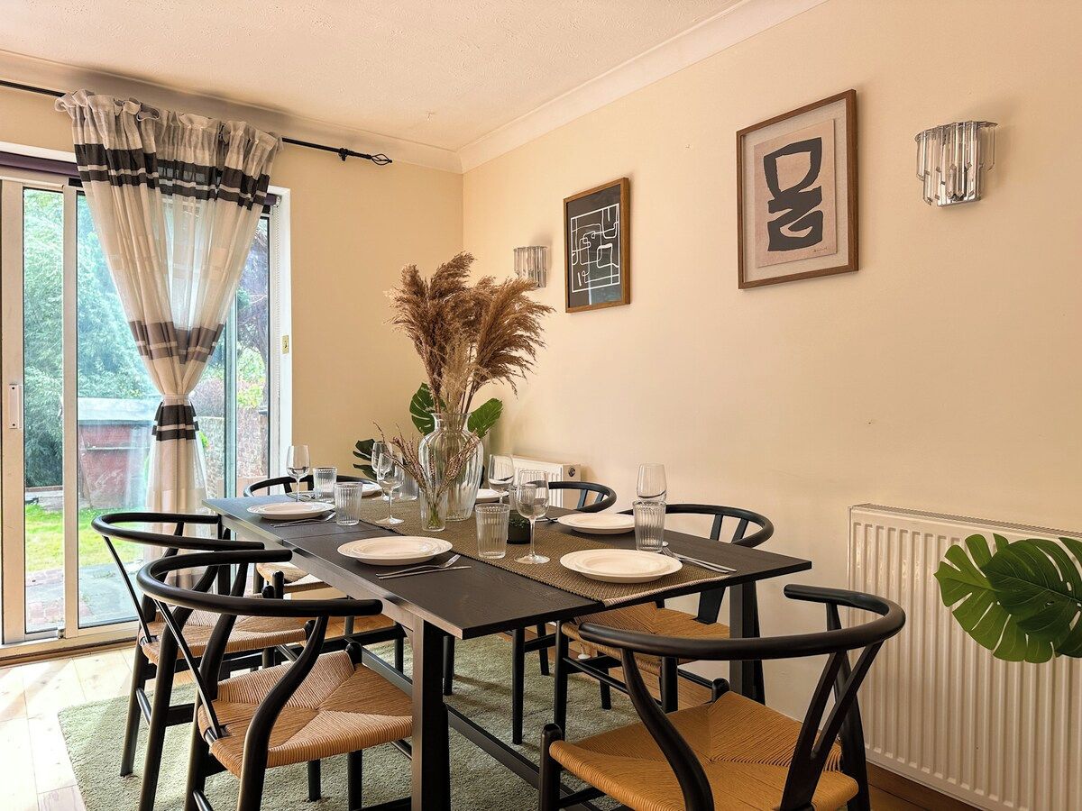 A dining area with a table set for four, chairs, a vase with dried plants, and framed artwork on the wall.