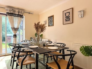 Un coin repas avec une table dressée pour quatre personnes, des chaises, un vase contenant des plantes séchées et des œuvres d’art encadrées accrochées au mur.