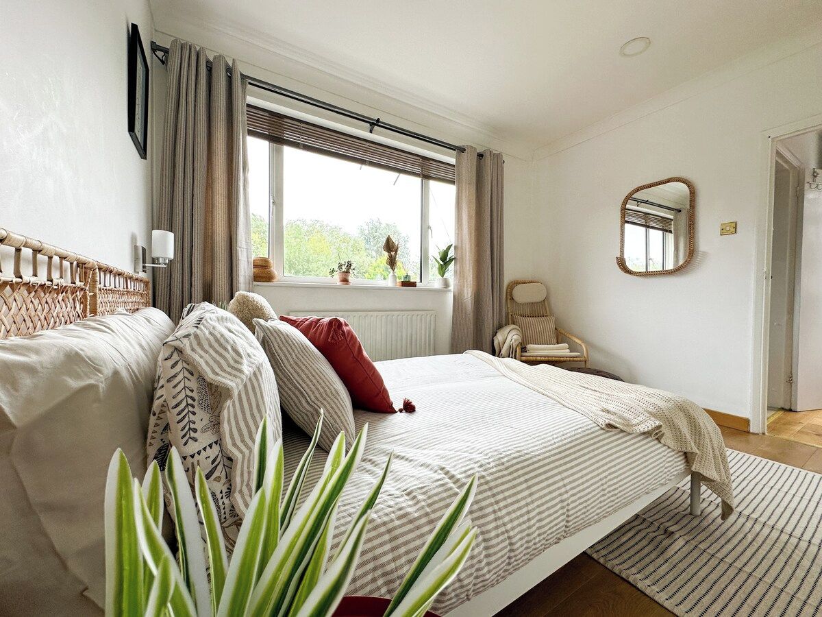 Ein Schlafzimmer mit einem Bett, einem Fenster mit Vorhängen, einem Sessel, einem Spiegel und einem Heizkörper.