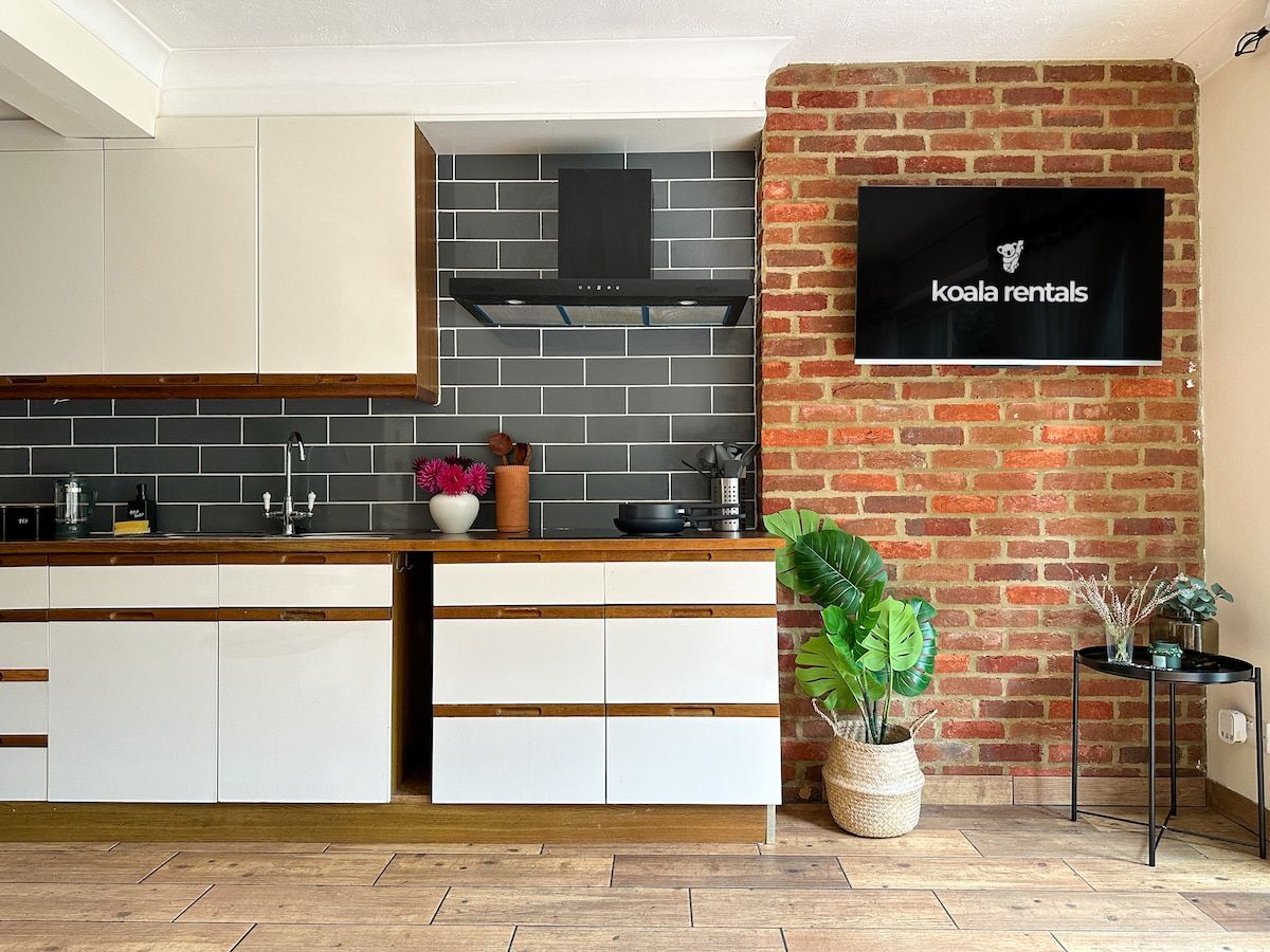 Une cuisine moderne avec des meubles blancs, un pare-feu noir et un mur d’accent en briques.