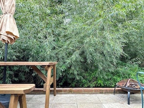 A wooden table and chair set outdoors with a metal chair and a table umbrella.