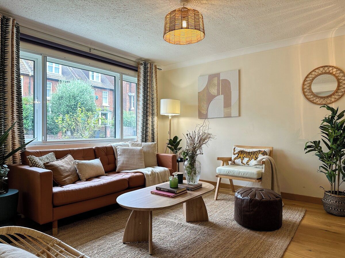 Un salon confortable avec un canapé, une table basse et un fauteuil. Il y a une fenêtre avec des rideaux, une lampe et une plante.