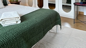 A bedroom with a bed, a green blanket, a bedside table with a lamp, a mirror, and a potted plant. - NEW The 82 | Spacious 3 Bed House on the River (Canterbury)