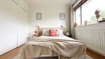 A bedroom with a bed, bedside tables, a window, and a radiator.