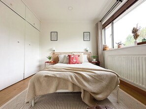 Une chambre à coucher avec un lit, des tables de chevet, une fenêtre et un radiateur.