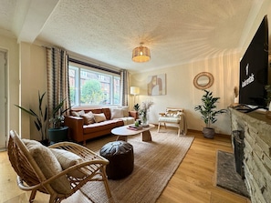 Un salon confortable avec un canapé, un fauteuil et un pouf, une cheminée et un téléviseur.