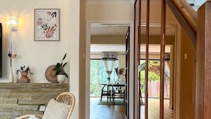 A spacious hallway with a wooden floor, a wicker chair, a stone fireplace, and a dining area with a table and chairs. - NEW The 82 | Spacious 3 Bed House on the River (Canterbury)