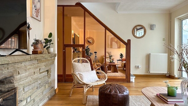 A cozy living room with a stone fireplace, a wicker chair, a wooden coffee table, and a view of the adjacent bedroom through a glass door. - NEW The 82 | Spacious 3 Bed House on the River (Canterbury)