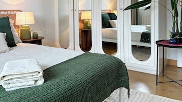 A hotel room with a bed, a nightstand, a mirror, and a potted plant.