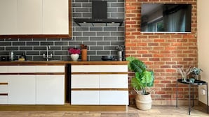 A modern kitchen with a brick accent wall, a flat-screen TV mounted above it, and a wooden countertop. - NEW The 82 | Spacious 3 Bed House on the River (Canterbury)