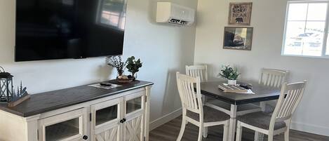 A dining area with a TV mounted on the wall, a wooden cabinet with glass doors, and a dining table with four chairs.
