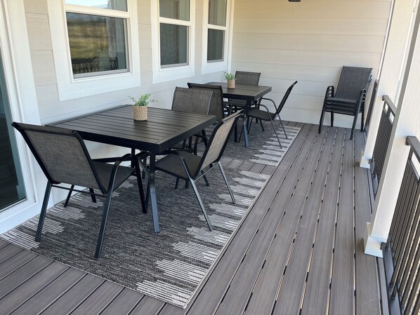 A covered patio with a dark wooden deck, a black metal table with four chairs, and a patterned rug.