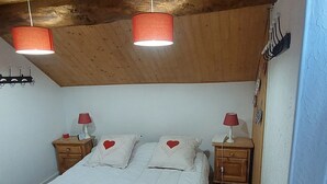 A bedroom with a wooden ceiling, a large bed with white bedding, two bedside tables with lamps, and a wall-mounted shelf.