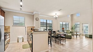 A spacious kitchen with a dining area, large windows, and a living room with a sofa and coffee table. - Bella Piazza Resort 3BR Charming Condo, By Disney (Davenport)