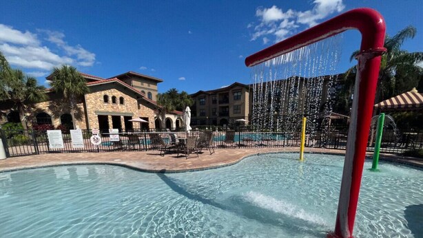 A swimming pool with clear water, surrounded by a poolside area with lounge chairs and a building in the background. - Bella Piazza Resort 3BR Charming Condo, By Disney (Davenport)