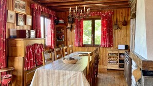 Een houten eetkamer met een lange tafel, stoelen, een kroonluchter en rode gordijnen.