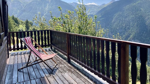 Een houten terras met een gestreepte stoel, met uitzicht op een bergachtig landschap.