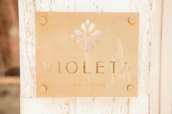 Ein Schild mit dem Namen „VIOLETA HOTEL BOUTIQUE“ und einem floralen Dekor.