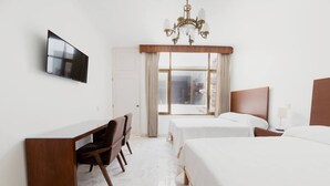 A hotel room with a flat-screen TV mounted on the wall, a wooden desk, two single beds, a chandelier, and a large window with curtains. - Violeta Hotel Boutique (Tepatitlan de Morelos)