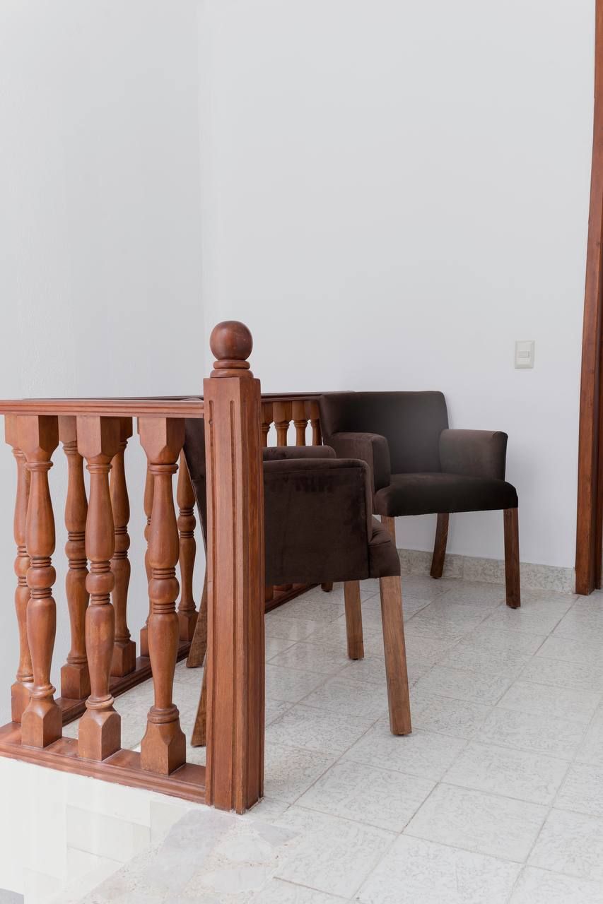 Une pièce avec un escalier en bois, un canapé brun foncé et un sol carrelé de couleur blanche.