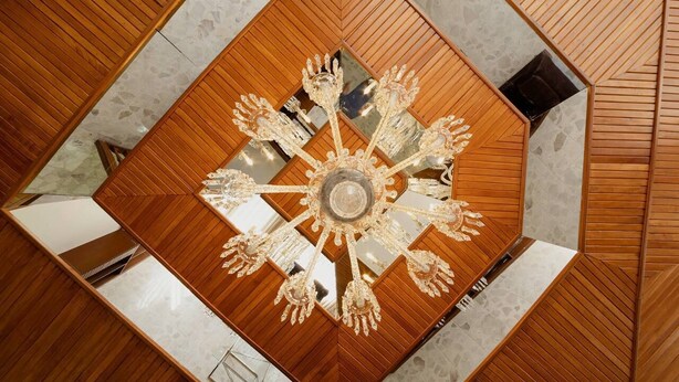 A chandelier with a central crystal piece and multiple arms, surrounded by a wooden floor with a geometric pattern. - Violeta Hotel Boutique (Tepatitlan de Morelos)