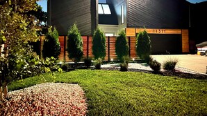 A modern building with a large garage door, a well-maintained lawn, and several trees. - Marvelous Modern Spacious 4-bedroom house  near interstate and Top Golf.  (Omaha)