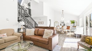 A spacious living room with a brown leather sofa, a glass coffee table, and a staircase leading to an upper level. - Marvelous Modern Spacious 4-bedroom house  near interstate and Top Golf.  (Omaha)