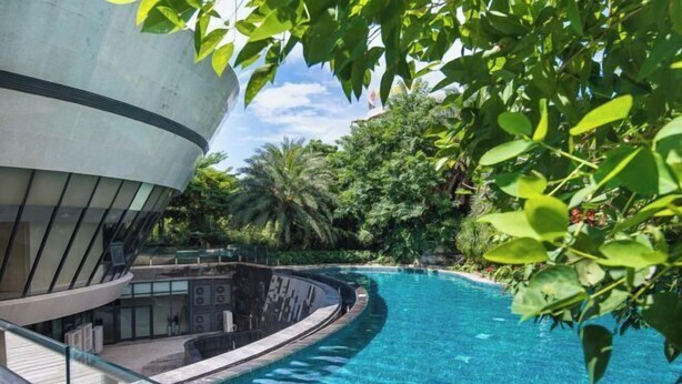 A modern building with a curved balcony overlooking a clear blue pool, surrounded by lush greenery. - Beihai Tuyu Oceanfront Scenic Apartment (Beihai)
