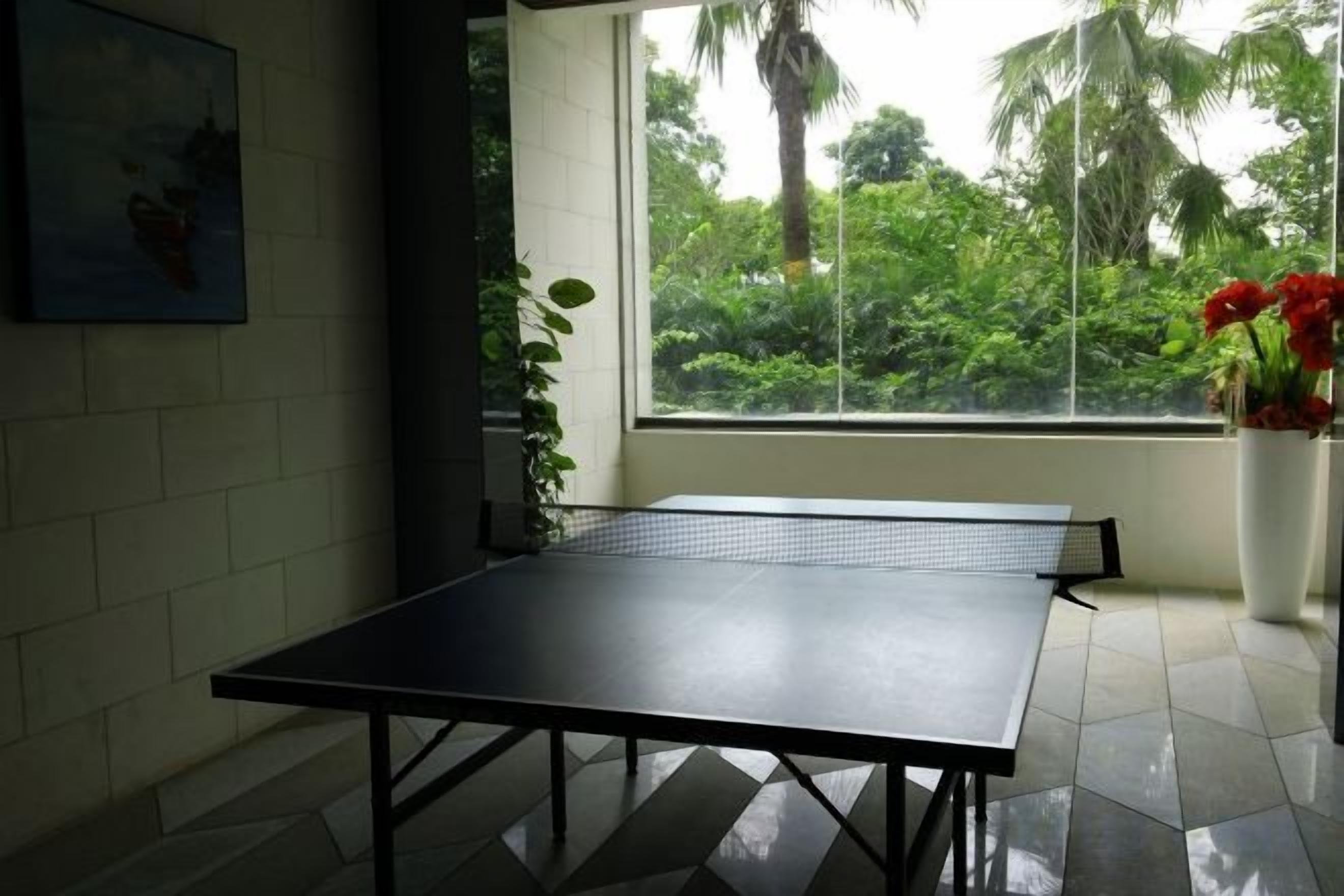 A ping pong table in a room with a window, a potted plant, and a painting on the wall.