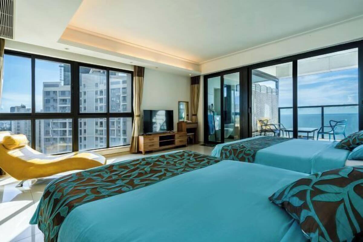A modern hotel room with two beds, a TV, a desk, and a balcony with a city view.