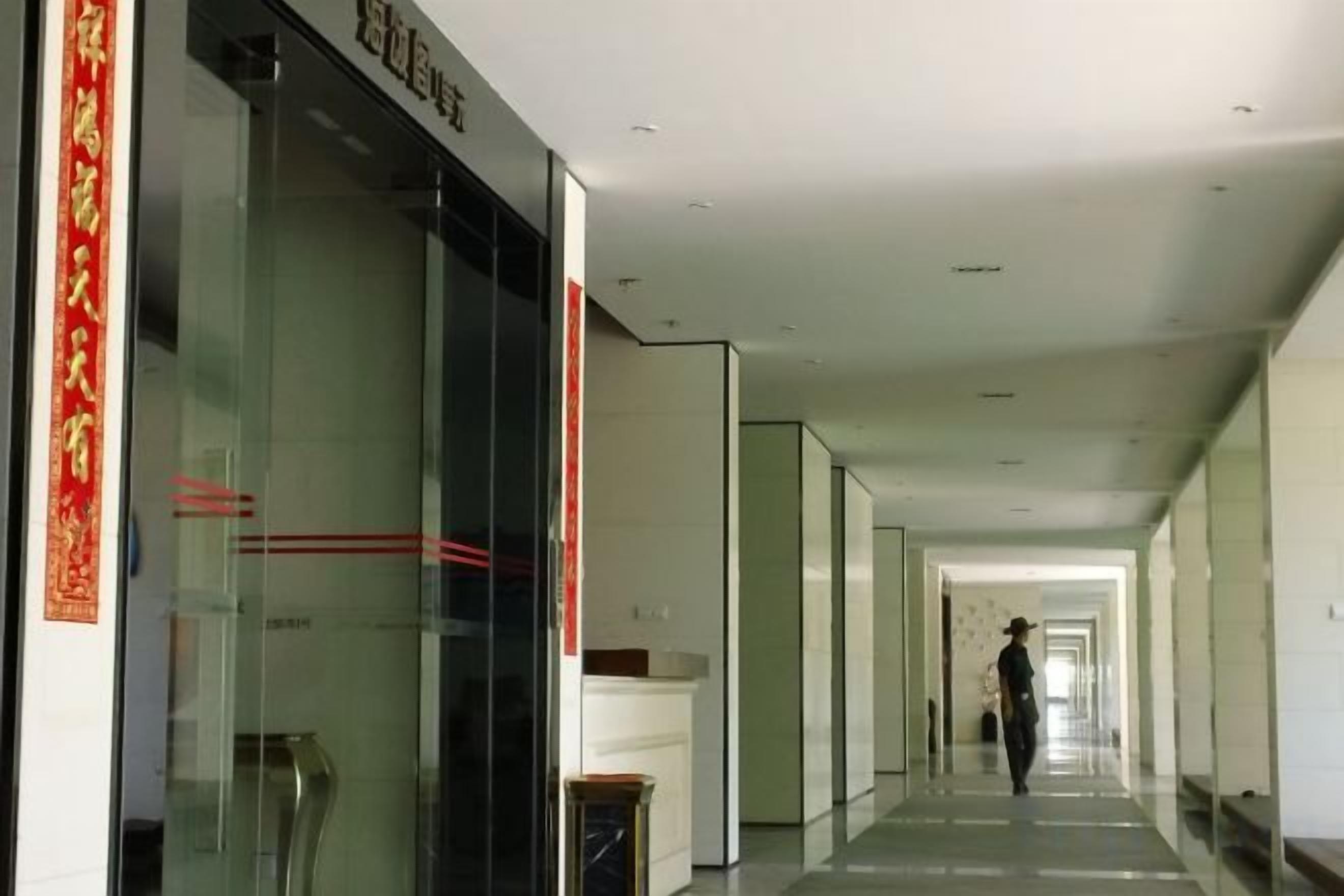 A corridor with glass doors on the left, a person walking in the distance, and a clean, modern interior.