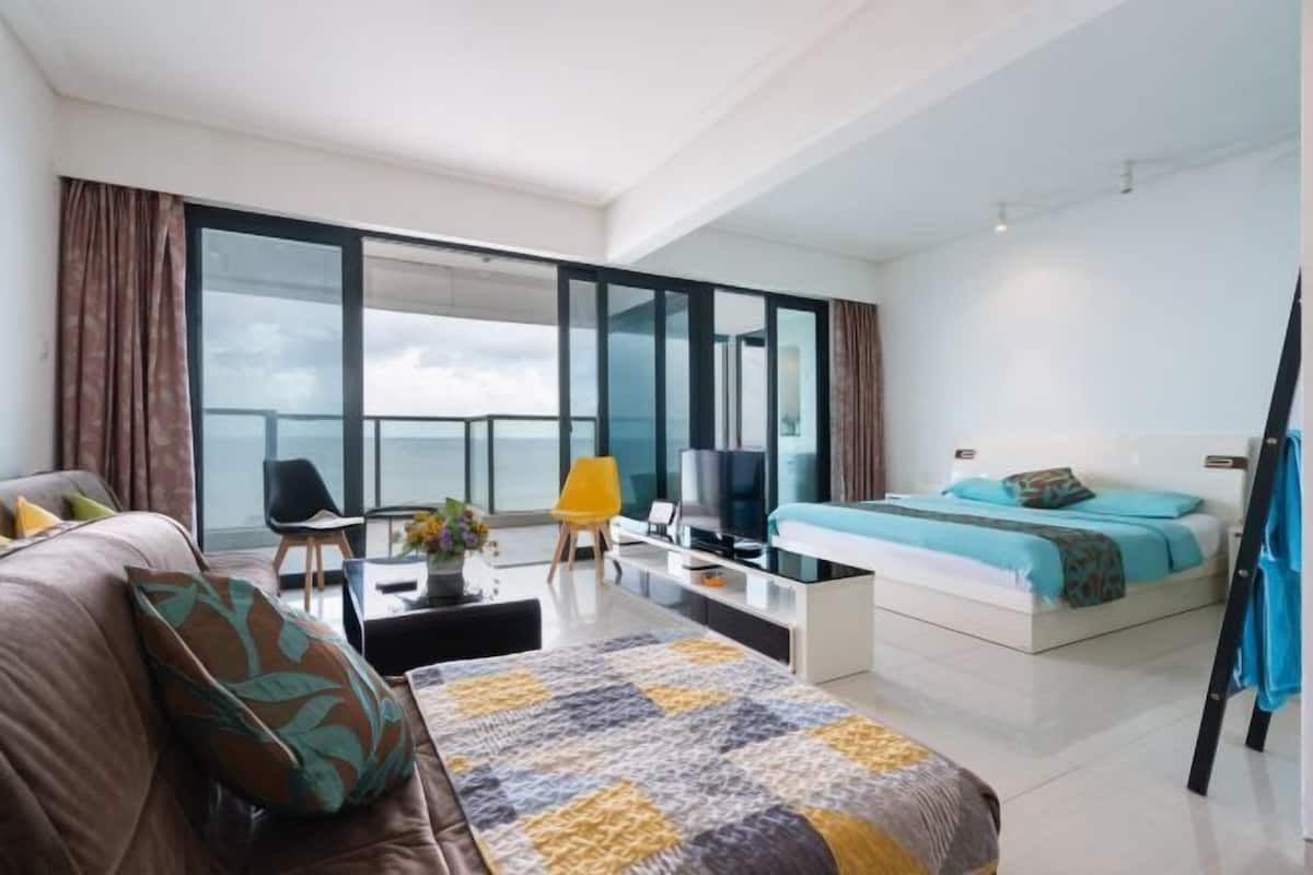 A modern hotel room with a large bed, a sofa, a TV, and a balcony with a view.