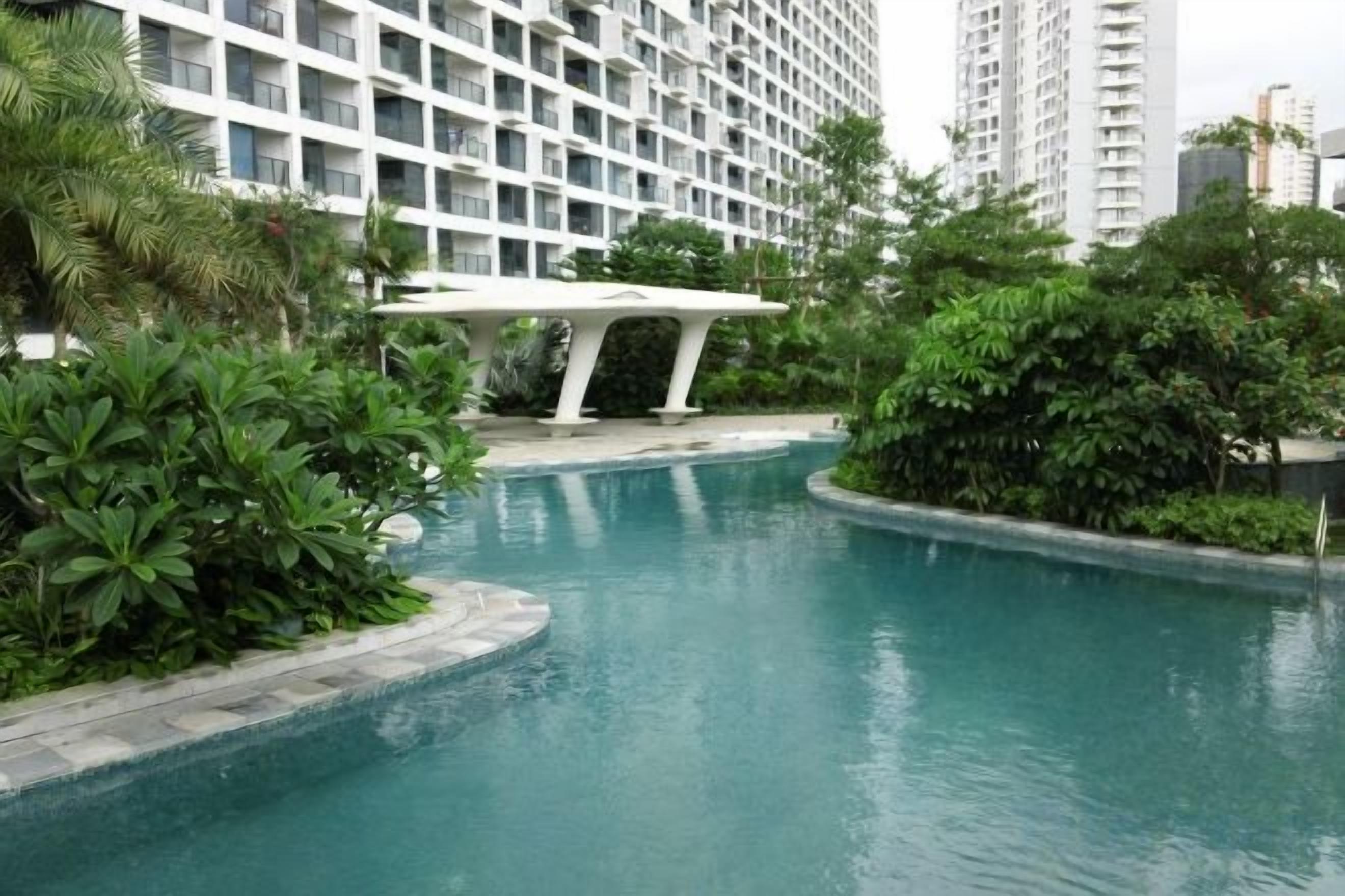A swimming pool with a white structure in the background, surrounded by greenery.